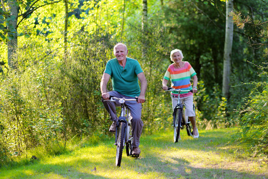 Happy healthy couple biking together in the forest. Seniors enjoying sunny day outdoors. Active retirement concept.