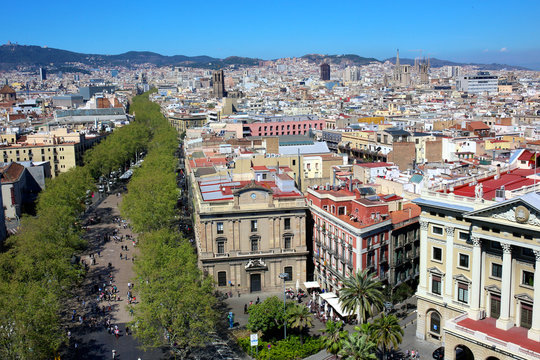 Las Ramblas, main touristic street in Barcelona, Spain. Aerial view from observation platform of Columbus monument. Sagrada Familia in the horizon. Family destination on summertime.