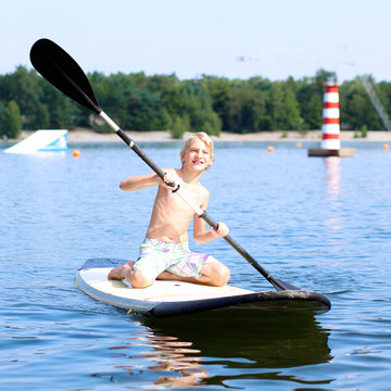 Adventurous boy learning to paddle on stand up board. Happy child, teenage schoolboy, having fun enjoying adventurous experience on the river on a sunny day during summer holidays