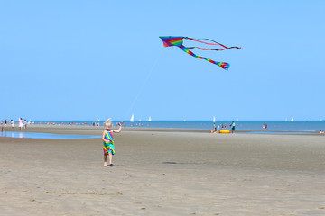 Cute toddler girl playing on the beach flying colorful kite. Child enjoying summer family vacation at the sea.