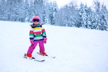 Fototapeta na wymiar Happy child enjoying vacation in Alpine resort. Little girl skiing in mountains. Active sportive toddler wearing helmet and glasses learning to ski. Winter sport for family. Skier racing in snow.