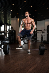 Fototapeta na wymiar Muscular Man Exercising Back With Barbell In Gym
