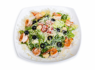 Caesar salad with shrimp, croutons, Parmesan cheese, tomatoes and olives. In a white plate, isolated on white background