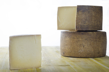 Whole wheel of sheep milk cheese over yellow wood.
