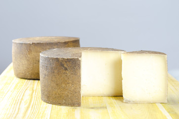 Whole wheel of sheep milk cheese over yellow wood.