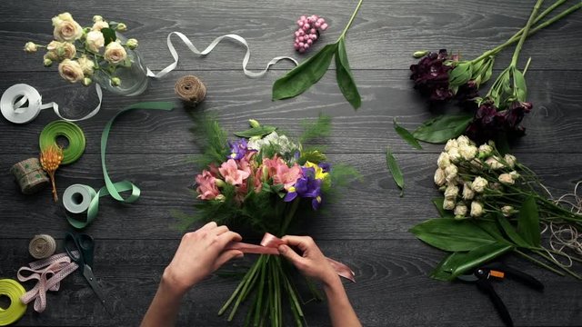 Girl's hands making bouquet of flowers over wood background. Slow motion. From above. Top view.