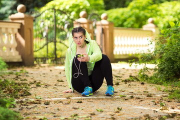 Young woman is listening to music on her headphones on smart phone while preparing for the exercise in a park.