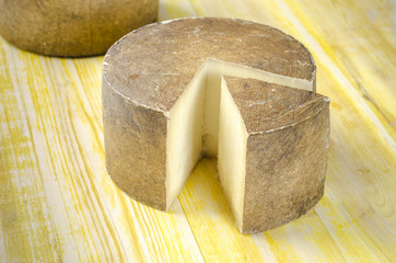 Whole wheel of sheep milk cheese over yellow wood.