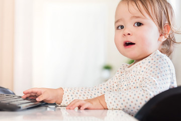 Fototapeta na wymiar Little toddler girl typing on her computer keyboard looking