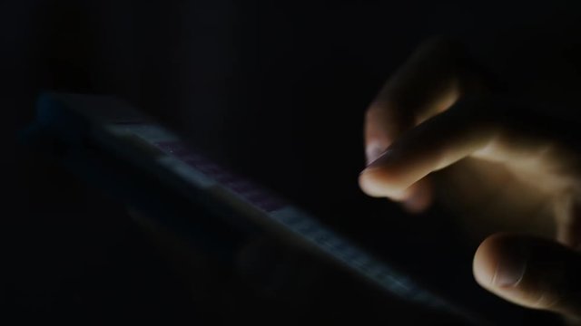 4K Hand using a digital touch screen tablet in the dark, in slow motion 