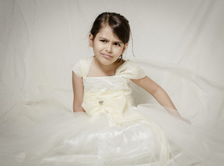 Fototapeta na wymiar Small girl in bridal dress sitting isolated inside studio