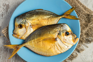 Fish.   Two smoked fish on a blue plate on a light wooden background.