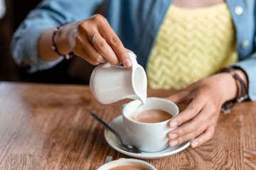 close up of woman hand pouring milk or cream to cup of coffee at