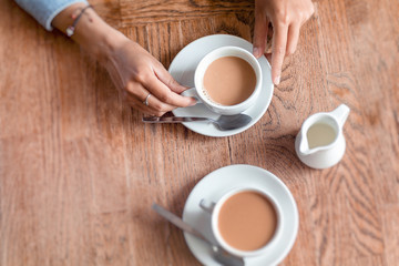 Two cups of coffee with woman hands on the wooden table in cafe