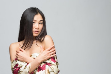 Portrait of fashion asian lady posing in spring or summer dress in studio. Beautiful woman with black hair demonstrating her gorgeous shoulders.
