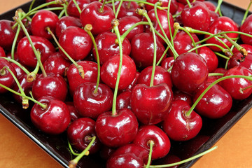 Ripe cherries in black porcelain plate on a wooden table