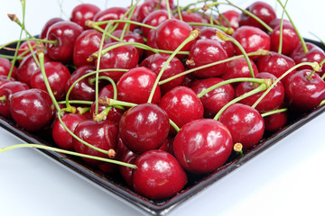 Ripe cherries in black porcelain plate on a white background isolated