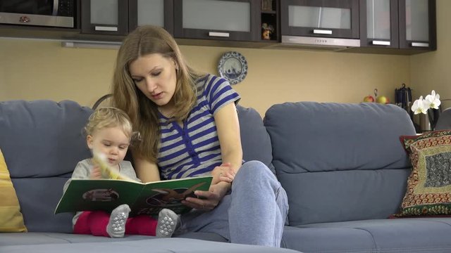 Woman and toddler child reading book together at home.