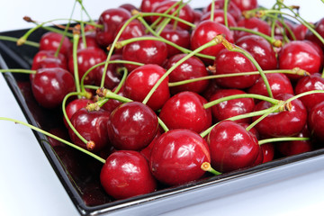 Ripe cherries in black porcelain plate on a white background isolated
