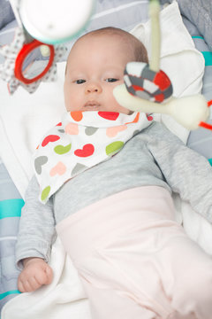Cute newborn baby girl in a rocking seat with toys hanging above
