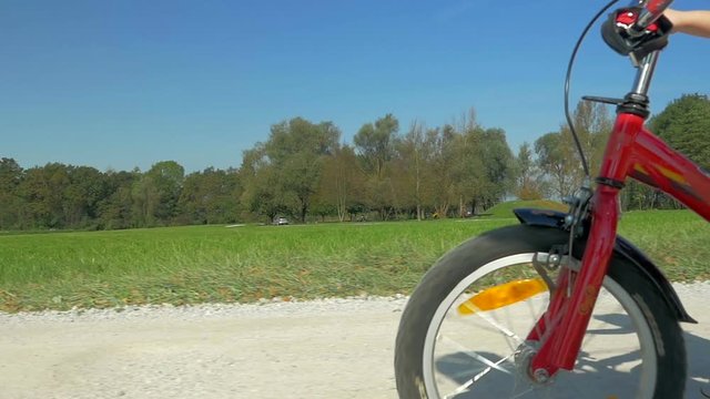 Low angle, dolly shot of a cute little girl on red bike and cycling in the park
