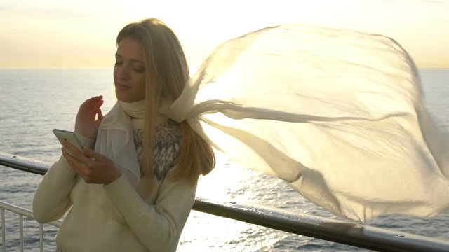 A young woman uses a smartphone to the deck of the liner in the sun. Slow Motion.