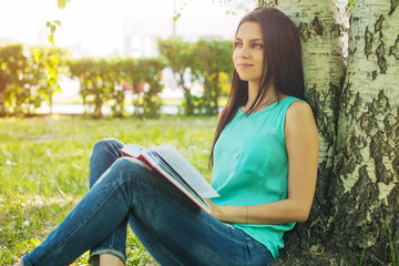 Obraz premium Girl sitting in grass, reading book in summer sun light