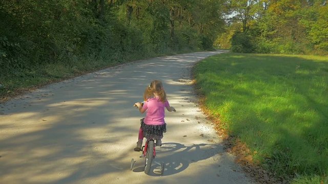 High angle, first person view, how ponytail little girl ride her red bike on macadam road
