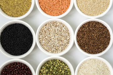 Different kinds of groats in small white bowls on white background