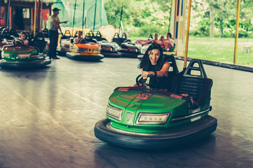 Cute young woman having fun in electric bumper car in amusement park