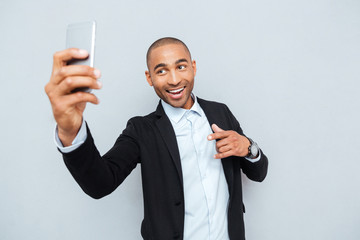 Young man making selfie photo on smartphone over gray background