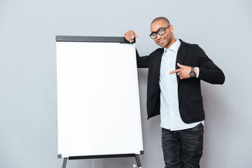 Happy african young man standing and pointing on blank flipchart