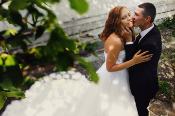 Naklejka premium Groom kisses bride's cheek delicately while they stand in an old
