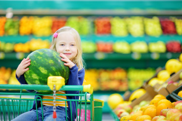 Fototapeta na wymiar Little girl holding a watermelon in a food store or a supermarket