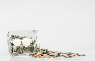 Coins spilled from glass jar, with copy space on white background