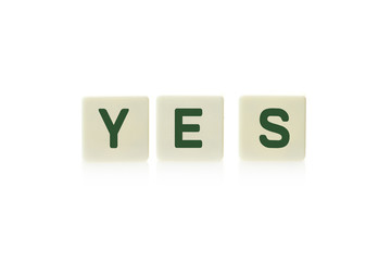 Word "Yes" on board game square plastic tile pieces, isolated on a white background.