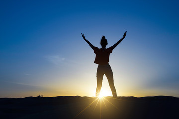 Silhouette of a woman standing in the sunlight with the arms up