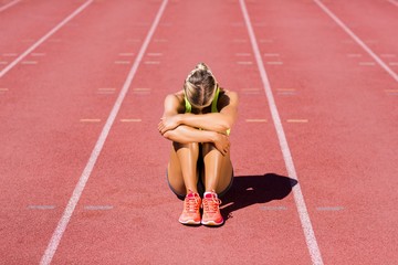 Upset female athlete sitting on running track