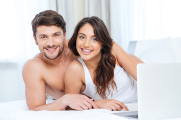 Smiling beautiful couple using laptop and looking at camera
