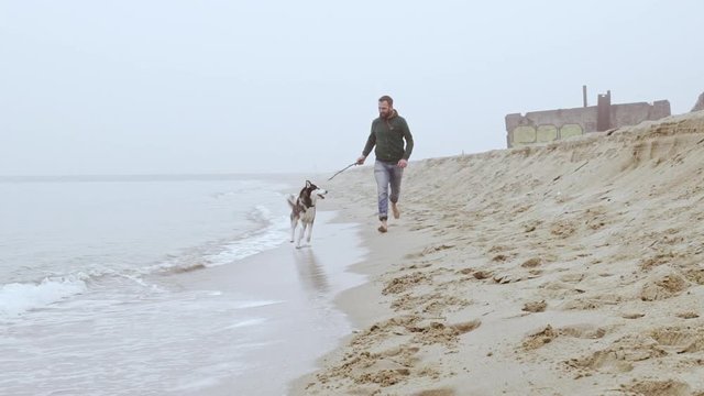 Handsome young man and his dog playing fetch at the beach. Slow motion