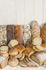 Całe chleby pełnoziarniste i kromki chleba na drewnianym stole w kompozycji z białymi deskami w tle