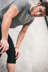 Obraz premium tired urban fitness man looking to the camera while resting leaning on wall. Sporty strong male exercising outdoors.