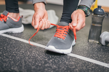 Running footwear close up. Gym indoor workout and fitness healthy concept. Male athlete tying sport...