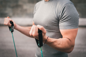 urban fitness man working out arm biceps using expander. Sporty strong male working out outdoors with elastic straps.