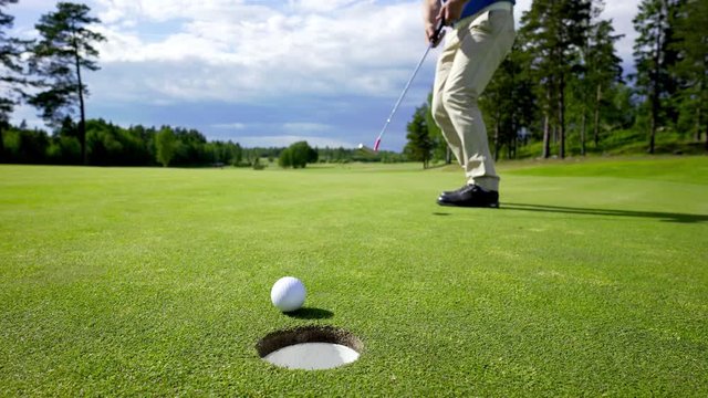 A man putting a golf ball into hole and making a victory gesture before picking up the ball