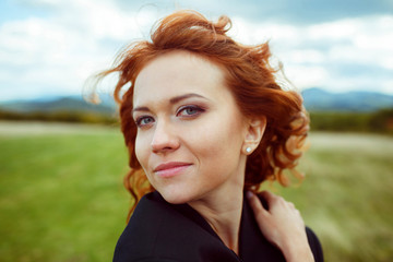 Fototapeta premium Lady with red curly hair looks stunning while wind blows along h