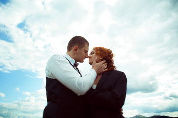 Groom kisses bride tenderly under deep blue sky with white cloud