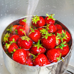 Bowl of organic strawberry in the sink under running water