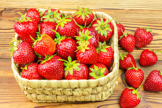 Full basket of ripe, organic strawberries on wooden table.