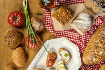 Pełnoziarnisty chleb, pomidory, szczypiorek i gotowe kanapki na drewnianym stole - obrazy, fototapety, plakaty